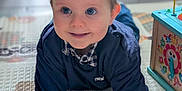 Ezra a rejoint le concours — aidez-le/la à gagner de superbes lots ! baby, blue_eyes, checkered, child, clothing, crawling, cute, floor, hands, happy, indoor, infant, navy_blue, person, play_mat, playtime, portrait, smiling, toy_box, young_child