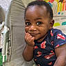 baby, child, infant, smiling, portrait, sitting, bouncer, baby_chair, playroom, rainbow, sun_decoration, toy, colorful, indoors, clothing, dark_skin, short_hair, hand_on_chin, happy, candid