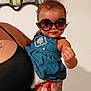 baby, child, sunglasses, blue_dress, tattoo, adult_hand, family_photos, wall, indoor, person, cute, fashion, portrait, holding, skin, hair, smile, eyewear, clothing, hand