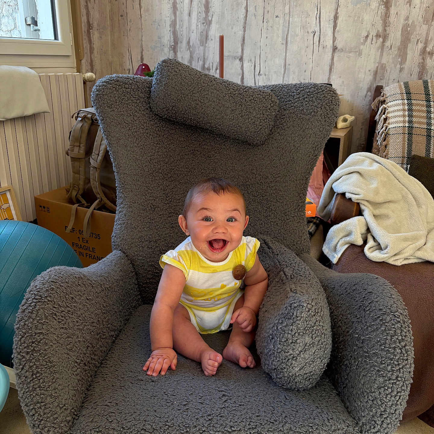 Pablo participe au concours pour gagner de l'argent avec cette photo : armchair, baby, child, clothing, cozy, cushion, floor, furniture, gray, happy, home, indoor, infant, person, plush, radiator, sitting, smiling, window, wooden_wall