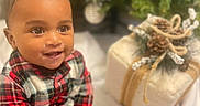 Jaymari joined the competition — help win amazing prizes! baby, blurred_background, child, cozy, cute, face, festive, gift, hands, happy, head, holiday_decor, indoor, person, pine_cones, plaid_clothing, portrait, sitting, smile, twine
