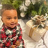 baby, blurred_background, child, cozy, cute, face, festive, gift, hands, happy, head, holiday_decor, indoor, person, pine_cones, plaid_clothing, portrait, sitting, smile, twine