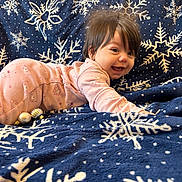 Ariana is registered to the contest to win money with this photo: baby, blanket, blue_blanket, child, christmas_ornaments, cozy, cute, decorations, face, festive, hair, happy, holiday_theme, indoor, infant, lying_down, pajamas, pink_clothing, smiling, snowflake_pattern
