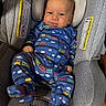 baby, infant, car_seat, onesie, blue_clothing, train_pattern, smile, face, head_support, fabric, child, young, indoor, seat, sitting, cute, comfortable, skin, person, footed_pajamas