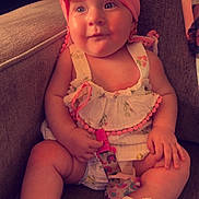 Willow is registered to the contest to win money with this photo: baby, child, infant, headband, pink, dress, pacifier, sitting, couch, footwear, white_booties, curious, indoors, soft_lighting, cute, chubby_arms, expression, comfortable, fabric, toy