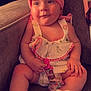 baby, child, infant, headband, pink, dress, pacifier, sitting, couch, footwear, white_booties, curious, indoors, soft_lighting, cute, chubby_arms, expression, comfortable, fabric, toy