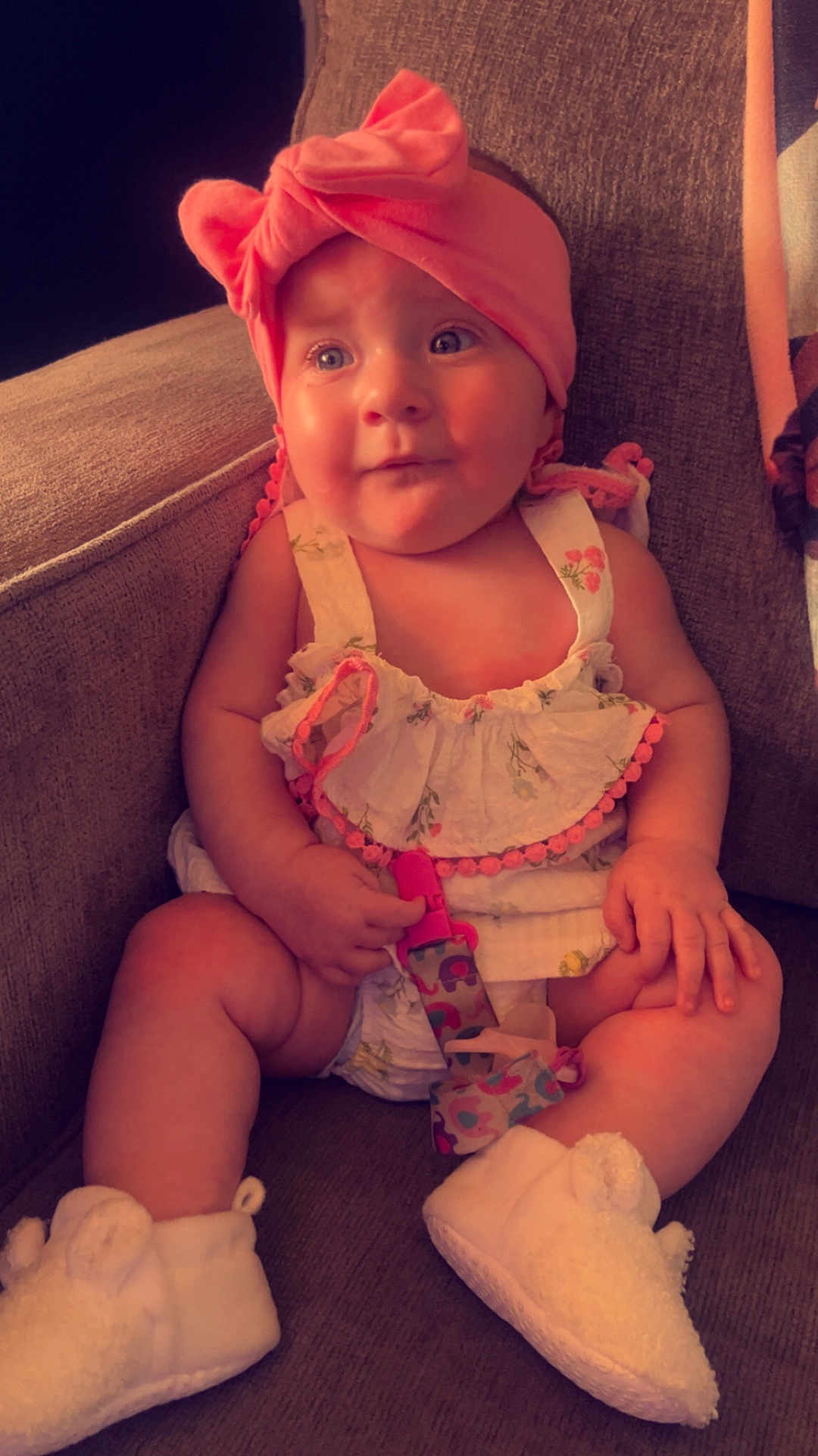 Willow is registered to the contest to win money with this photo: baby, child, infant, headband, pink, dress, pacifier, sitting, couch, footwear, white_booties, curious, indoors, soft_lighting, cute, chubby_arms, expression, comfortable, fabric, toy