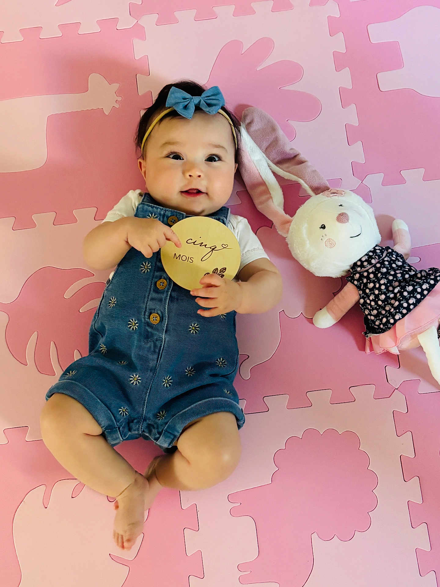 Mia-Maï a rejoint le concours — aidez-le/la à gagner de superbes lots ! animal_shapes, baby, baby_clothing, blue_bow, child, cinq_mois, cute, denim_romper, happy, headband, indoor, infant, lying_down, pink_puzzle_mat, plush_bunny, portrait, smiling, soft_toy, toy, wooden_sign