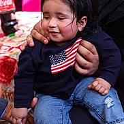Gurbaaz Singh is registered to the contest to win money with this photo: american_flag, blue, bottle, child, clothing, coca_cola, cute, face, flag, hair, hand, holding, indoor, jeans, person, red, sitting, smile, sweater, toddler
