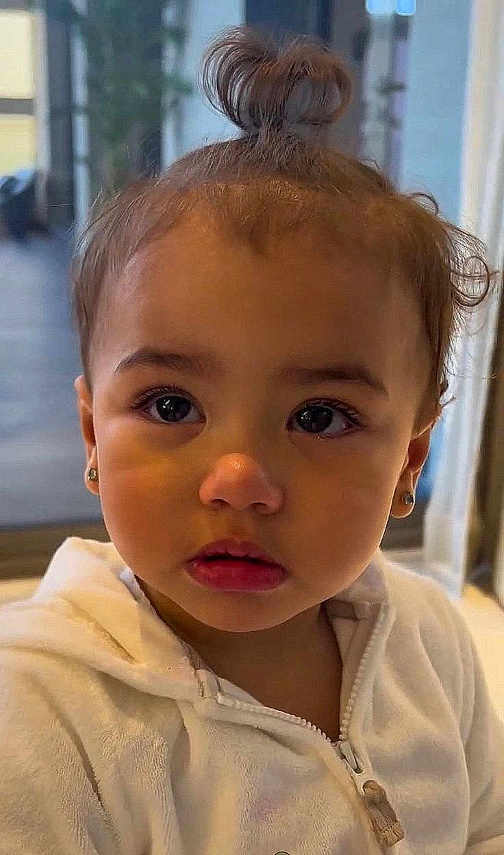 Samira a rejoint le concours — aidez-le/la à gagner de superbes lots ! toddler, child, face, portrait, indoors, white_hoodie, topknot, cute, expression, young_child, ears, zipper, hair, big_eyes, skin, nose, mouth, eyebrows, indoor_lighting, soft_background