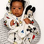 baby, child, mickey_mouse, plush_toy, robe, soft_fabric, cute, indoor, portrait, infant, foot, hand, face, expressionless, cozy, pillow, writing, black_hair, cuddly, wrapped