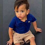 Ares joined the competition — help win amazing prizes! child, toddler, boy, sitting, blue_polo, beige_shorts, shorts, curious, expression, indoors, dark_background, cute, portrait, young_child, hands, face, hair, looking_up, casual_clothing, small