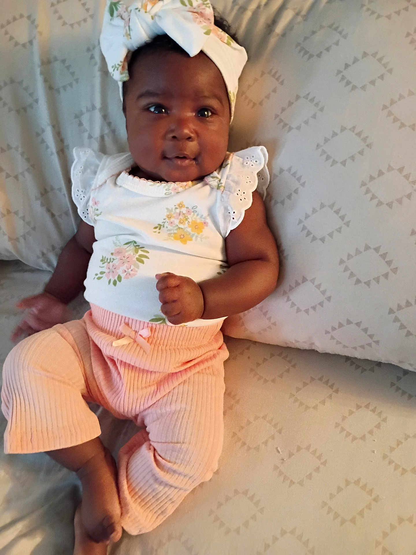 Jalaisha is registered to the contest to win money with this photo: baby, infant, child, headwrap, floral, pink_pants, cushion, patterned, comfortable, indoor, portrait, smiling, cute, clothing, fabric, person, sitting, soft_lighting, closeup, happy