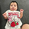 baby, cartoon_characters, child, clothing, cute, diaper, face, gray_background, hair, hand, hello_kitty, indoors, infant, lying_down, portrait, skin, soft_lighting, strawberry, tshirt, young_child