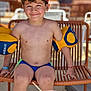 beverage, boy, casual, chair, child, curly_hair, drink, floaties, happy, outdoor, playful, portrait, red_cap, relaxation, seat, smiling, summer, sunny, swimwear, water_fun