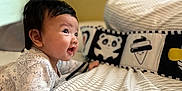 Olivia joined the competition — help win amazing prizes! baby, infant, tummy_time, bed, striped_bedspread, pillow, cartoon_pillow, cute, child, indoors, smiling, black_hair, sleepwear, cozy, curious, young_child, soft_lighting, portrait, bedroom, resting