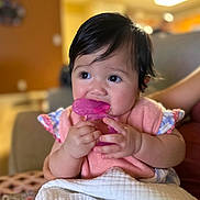 Olivia joined the competition — help win amazing prizes! baby, child, teething_toy, pink, blanket, indoor, curly_hair, cute, infant, person, holding, sitting, soft_lighting, portrait, closeup, clothing, hand, face, cheeks, expression