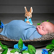Tristan is registered to the contest to win money with this photo: baby, sleeping, blanket, blue, plush_toy, bunny, flower, artificial_flower, green_leaves, bowl, fur_rug, cozy, portrait, infant, peaceful, indoor, decor, cute, resting, child