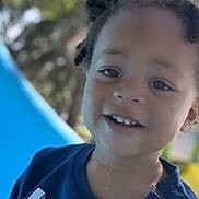 Haylo joined the competition — help win amazing prizes! child, toddler, smiling, portrait, outdoor, playground, slide, trees, sunlight, curly_hair, blue_shirt, shirt, face, head, eyes, teeth, happy, photograph, phone_screenshot, daytime