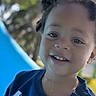 child, toddler, smiling, portrait, outdoor, playground, slide, trees, sunlight, curly_hair, blue_shirt, shirt, face, head, eyes, teeth, happy, photograph, phone_screenshot, daytime
