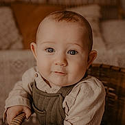 Eden a rejoint le concours — aidez-le/la à gagner de superbes lots ! baby, child, face, eyes, clothing, overalls, shirt, hands, wicker, chair, cushion, pillow, home_interior, portrait, cute, smile, infant, sitting, warm_tones, indoor