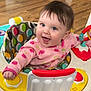 baby, child, smiling, play, activity_center, pink_onesie, cherry_pattern, toy, indoor, happy, face, colorful, furniture, floor, person, infant, cute, expression, joy, hands