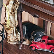 Thumper joined the competition — help win amazing prizes! puppy, sleeping, toy_truck, wooden_floor, wooden_table, statue, decor, indoor, cozy, resting, black_and_tan, dog, furniture, vintage_toy, quiet, peaceful, home, floor, small, cute