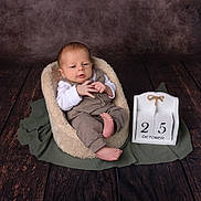 Elijah joined the competition — help win amazing prizes! baby, infant, child, plush_seat, brown_outfit, white_shirt, wooden_calendar, october, date, floor, wooden_floor, texture, portrait, indoor, cozy, cute, hands, feet, expression, background