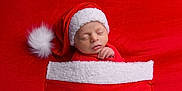 Elijah joined the competition — help win amazing prizes! baby, newborn, santa_hat, red_clothing, blanket, sleeping, holiday, christmas, cute, infant, face, portrait, soft_texture, wrapped, cozy, hands, red_background, holiday_theme, resting, peaceful