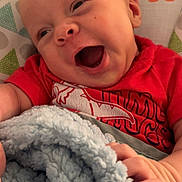 Jericho is registered to the contest to win money with this photo: baby, infant, child, smiling, laughing, portrait, close_up, red_shirt, blanket, fluffy_blanket, sitting, baby_seat, indoors, patterned_background, happy, face, hands, family_photo, cute, photography