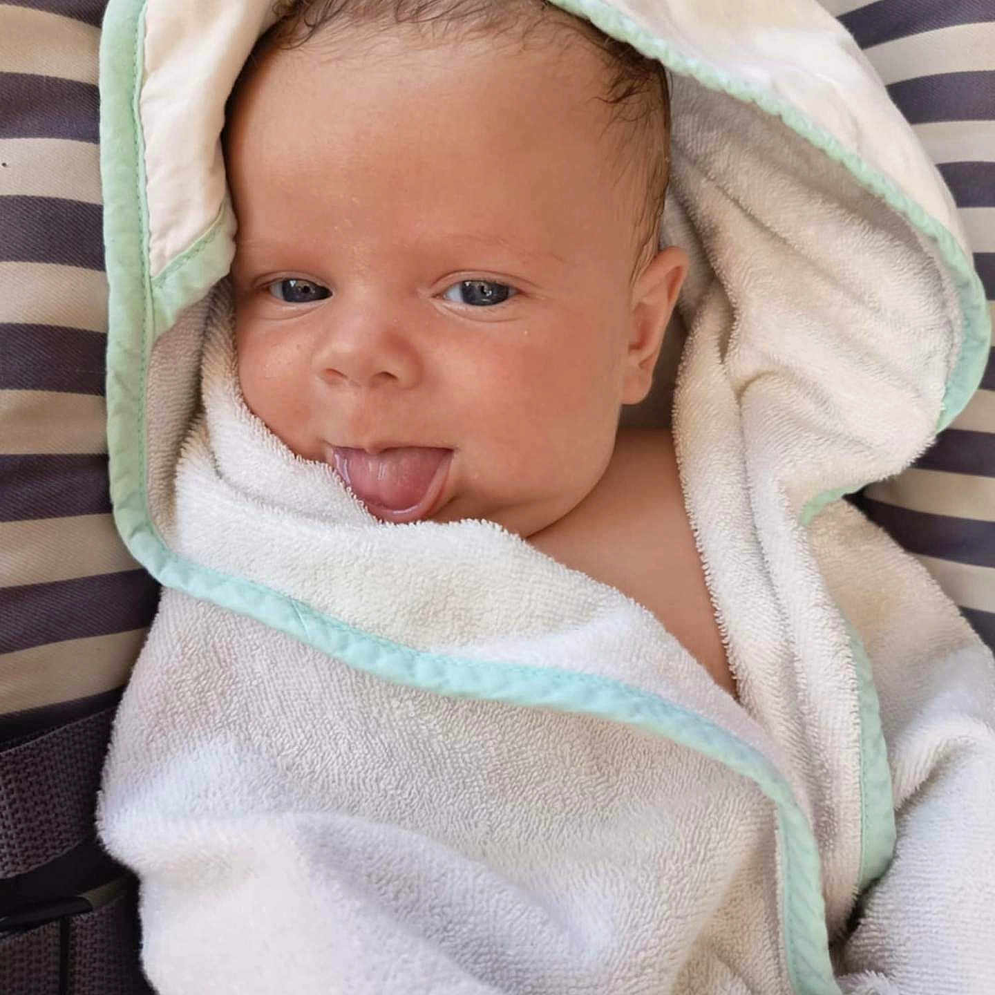 Giorgio participe au concours pour gagner de l'argent avec cette photo : baby, blanket, blue_eyes, child, cute, face, hooded_towel, indoors, infant, person, playful, relaxed, skin, smiling, soft_texture, striped_cushion, tongue_out, towel, wrapped, young