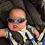 Ronan joined the competition — help win amazing prizes! baby, child, sunglasses, car_seat, medical_tube, breathing_tube, straps, infant, cute, tongue_out, camouflage_clothing, seatbelt, black, blue, medical_device, happy, portrait, indoors, person, accessory