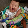 Ronan is registered to the contest to win money with this photo: baby, infant, yawning, baby_seat, toy, colorful, medical_tube, indoors, carpet, footwear, white_clothing, plastic, child, cute, human, sitting, playful, comfort, healthcare, young