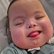 Ronan is registered to the contest to win money with this photo: baby, face, tongue, chubby_cheeks, smiling, close_up, infant, child, seatbelt, clothing, cushion, resting, cute, happy, indoors, person, skin, young_child, expression, head