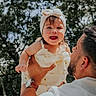Everly is registered to the contest to win money with this photo: baby, child, man, father, outdoor, smiling, happy, holding, headband, nature, tree, sunlight, portrait, family, love, joy, cute, clothing, person, playful