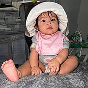 Everly joined the competition — help win amazing prizes! baby, child, infant, hat, pink_bib, sitting, indoors, toes, hand, foot, blanket, curious, wide_eyes, soft_texture, playful, person, young_child, clothing, cute, portrait