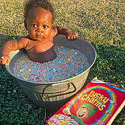 Cotie joined the competition — help win amazing prizes! baby, child, bucket, cereal, lucky_charms, milk, outdoor, grass, sunlight, box, colorful, marshmallows, metal, curly_hair, expression, puzzled, playful, water, holding, sitting