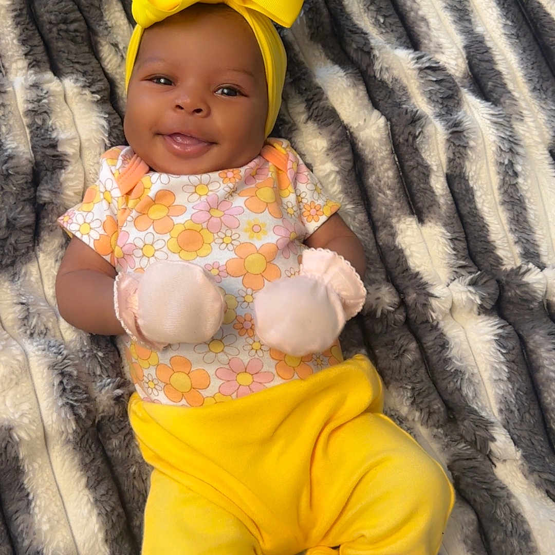 Reigh'Lynn is registered to the contest to win money with this photo: baby, smile, yellow_bow, mittens, floral_top, yellow_pants, blanket, striped_blanket, infant, happy, lying_down, cute, headband, cozy, soft, child, portrait, apparel, indoor, person