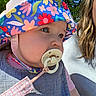baby, child, pacifier, hat, floral_pattern, outdoor, sunlight, person, face, closeup, blue, pink, clothing, nature, trees, woman, adult, portrait, headwear, summer