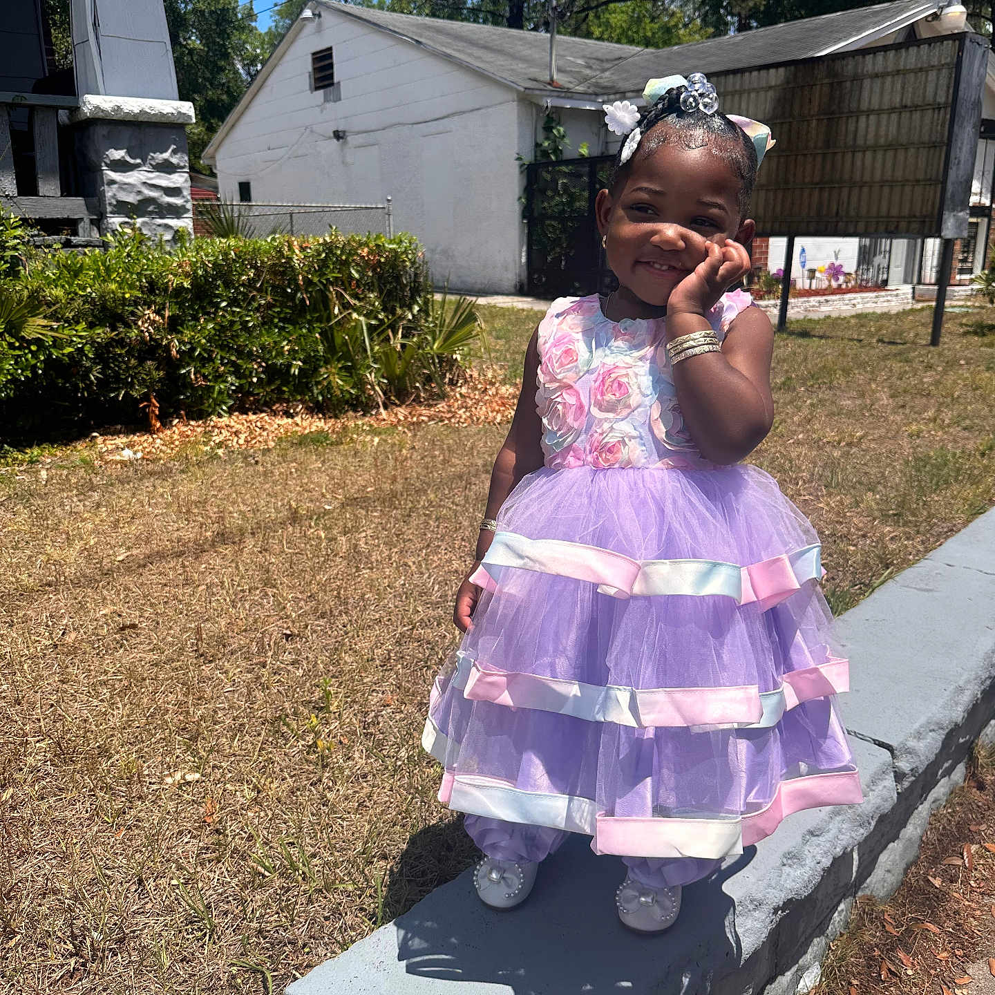 Jailah is registered to the contest to win money with this photo: child, girl, dress, purple, pink, outdoor, sunny, smiling, concrete, grass, hedge, blue_sky, shoes, bracelet, hair_bow, cute, happy, portrait, daylight, standing