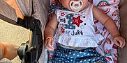Nyella is registered to the contest to win money with this photo: baby, pacifier, stroller, blanket, rainbow_pattern, flower_hair_clip, clothing, blue_shorts, white_top, smiling, infant, child, cute, comfortable, outdoor, person, legs, hand, soft_toy, fabric