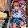 baby, pacifier, stroller, blanket, rainbow_pattern, flower_hair_clip, clothing, blue_shorts, white_top, smiling, infant, child, cute, comfortable, outdoor, person, legs, hand, soft_toy, fabric