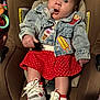 baby, denim_jacket, pacifier, car_seat, red_skirt, polka_dot, sneakers, child, indoor, cute, clothing, footwear, seated, expression, toy, infant, person, face, hair, apparel