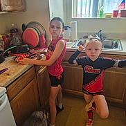 Novaeh is registered to the contest to win money with this photo: child, children, kitchen, cutting_board, strawberries, dog, floor, countertop, window, sink, cup, dish_rack, paper_towel, plant, flag, blouse, shorts, shoes, posing, playful