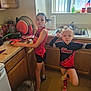 child, children, kitchen, cutting_board, strawberries, dog, floor, countertop, window, sink, cup, dish_rack, paper_towel, plant, flag, blouse, shorts, shoes, posing, playful