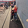 child, children, indoor, gym, people, crowd, wall, carpet, floor, chairs, spectators, casual_clothing, jeans, sneakers, sportswear, pointing, smiling, group, event, young
