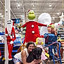 woman, dog, store, holiday_decorations, grinch, skeleton_santa, christmas, smiling, indoor, shopping_aisle, festive, puppy, hugging, costume, large_dog, toy_figures, celebration, happy, people, seasonal