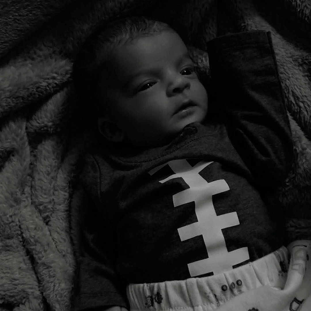 Rylan joined the competition — help win amazing prizes! baby, infant, black_and_white, blanket, clothing, face, soft_texture, lying_down, patterned_pants, football_design, cute, portrait, young_child, sleepwear, indoors, peaceful, small_hand, expression, cozy, resting