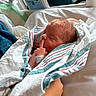 newborn, baby, hospital, blanket, bed, sleeping, finger, person, adult, hospital_bed, wrapped, peaceful, cute, infant, hand, smile, parent, medical, indoors, tender