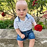 Patrick is registered to the contest to win money with this photo: baby, child, infant, portrait, sitting, outdoor, garden, rose, flower, red_flower, greenery, foliage, nature, smiling, wide_eyed, blue_eyes, plaid_shirt, denim_shorts, barefoot, adult_hand